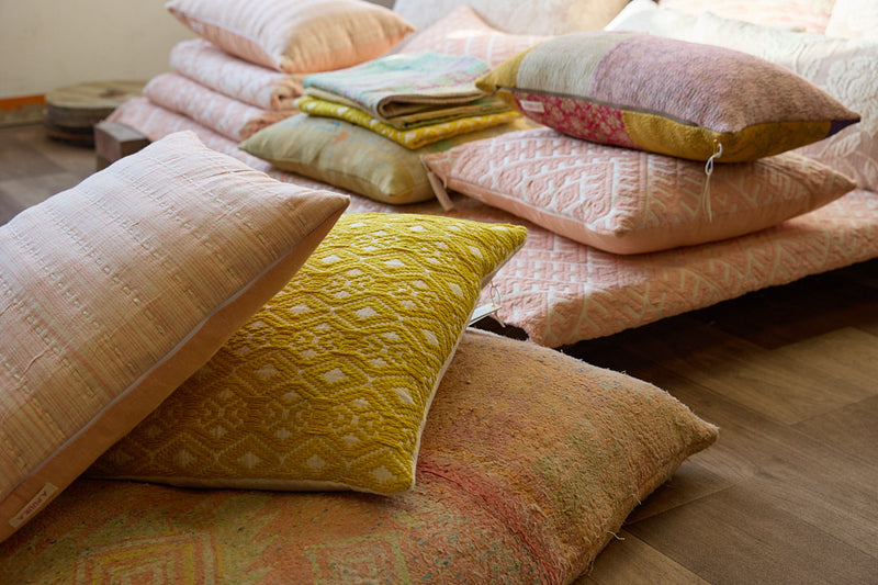 A pile of cushions, plaids and textiles in yellow and peach tones displayed in ATELIER A.PUUR.A shop 